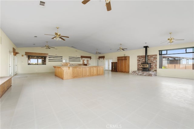 unfurnished living room featuring a healthy amount of sunlight, ceiling fan, a wood stove, and light tile floors