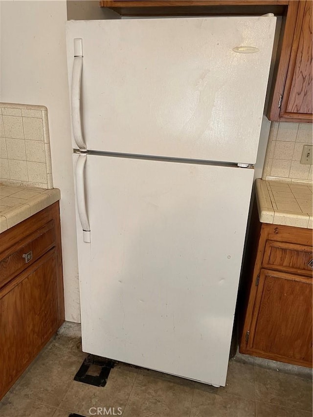 kitchen with decorative backsplash, white refrigerator, and tile countertops