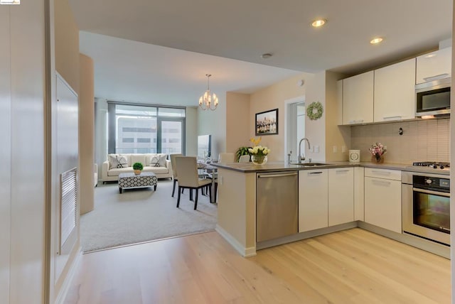 kitchen with light wood-type flooring, appliances with stainless steel finishes, kitchen peninsula, decorative light fixtures, and tasteful backsplash