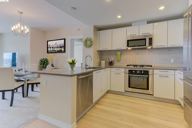 kitchen with stainless steel appliances, kitchen peninsula, decorative light fixtures, sink, and tasteful backsplash