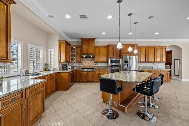 kitchen with a kitchen bar, appliances with stainless steel finishes, ornamental molding, a center island with sink, and decorative light fixtures