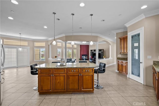 kitchen featuring decorative light fixtures, a kitchen island with sink, crown molding, and sink