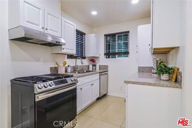 kitchen featuring sink, light stone countertops, light tile patterned floors, white cabinetry, and stainless steel appliances