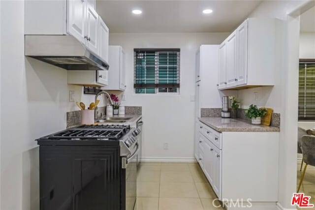 kitchen featuring light tile patterned floors, white cabinetry, stainless steel gas range oven, and sink