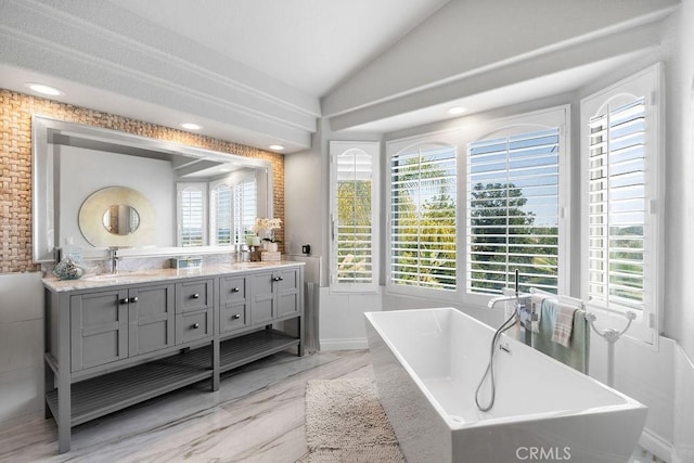 bathroom featuring vanity, lofted ceiling, a tub to relax in, and a healthy amount of sunlight