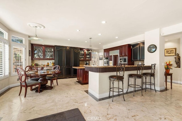 kitchen with built in appliances, decorative backsplash, decorative light fixtures, a kitchen bar, and kitchen peninsula