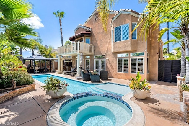 rear view of house featuring a gazebo, a patio area, a balcony, and a pool with hot tub