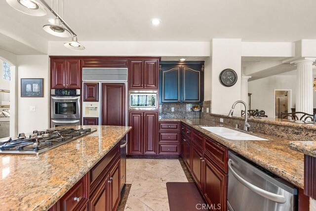 kitchen with sink, hanging light fixtures, built in appliances, light stone countertops, and decorative columns