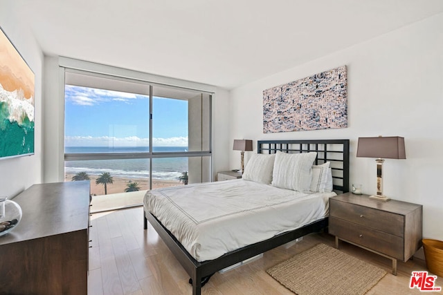 bedroom with expansive windows, hardwood / wood-style flooring, and a water view