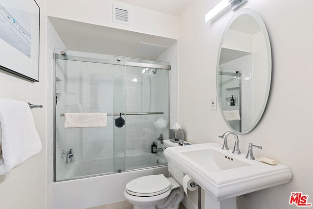 full bathroom featuring sink, combined bath / shower with glass door, and toilet