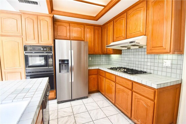 kitchen featuring appliances with stainless steel finishes, tile counters, decorative backsplash, and ornamental molding