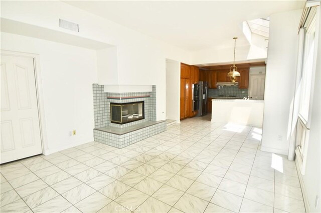 kitchen featuring stainless steel refrigerator, backsplash, light tile patterned floors, kitchen peninsula, and hanging light fixtures