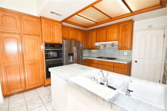 kitchen featuring crown molding, tile counters, decorative backsplash, and stainless steel appliances