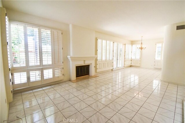 unfurnished living room with a healthy amount of sunlight, an inviting chandelier, and light tile patterned flooring