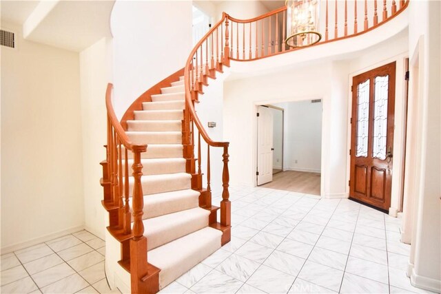 entryway featuring an inviting chandelier, a towering ceiling, and light tile patterned flooring