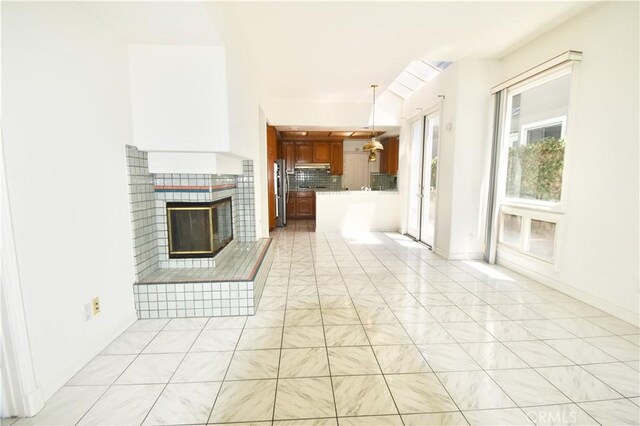 interior space featuring a fireplace, stainless steel refrigerator, backsplash, decorative light fixtures, and kitchen peninsula