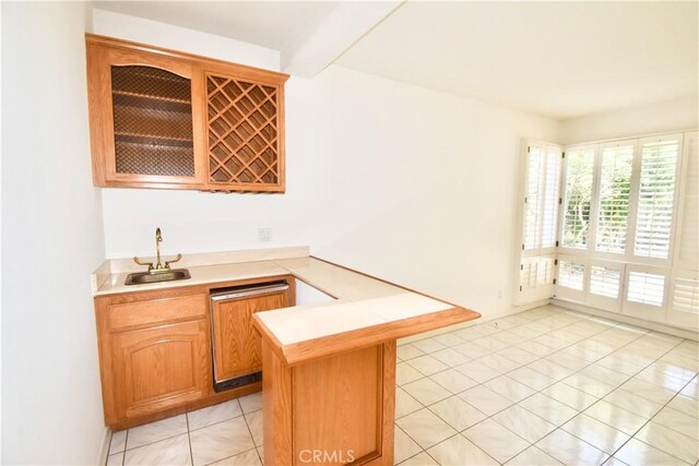 kitchen with light tile patterned floors, stainless steel dishwasher, kitchen peninsula, and sink