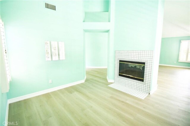 unfurnished living room with light wood-type flooring, a high ceiling, and a tile fireplace