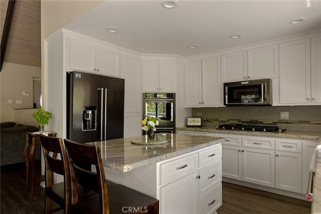 kitchen with white cabinetry, light stone counters, a breakfast bar area, a kitchen island, and appliances with stainless steel finishes