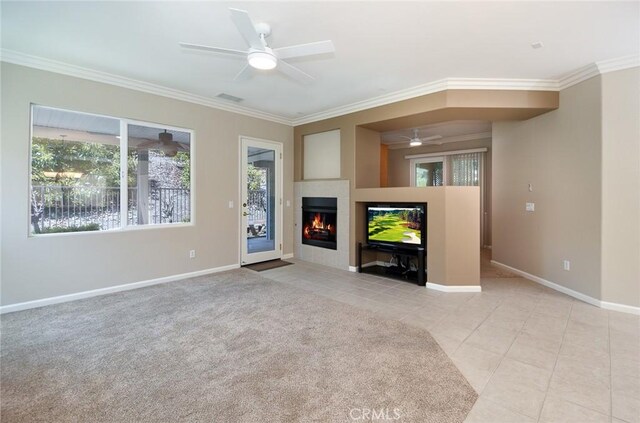 unfurnished living room featuring a tile fireplace, light carpet, ceiling fan, and ornamental molding