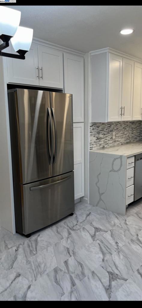 kitchen with white cabinetry, backsplash, light tile flooring, and stainless steel appliances