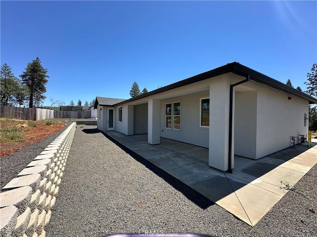 view of side of property with a patio, fence, and stucco siding