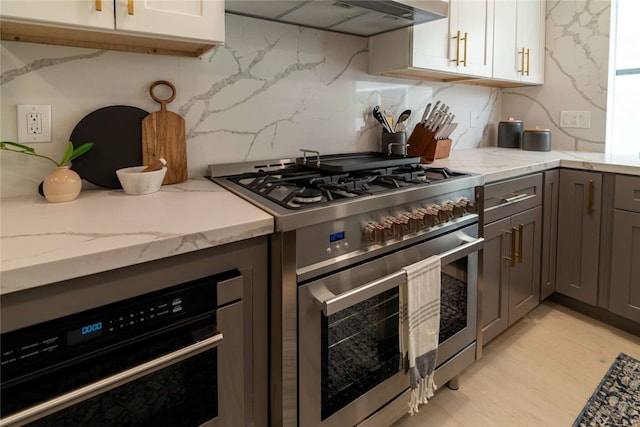 kitchen with stainless steel appliances, white cabinets, light stone countertops, light hardwood / wood-style floors, and premium range hood