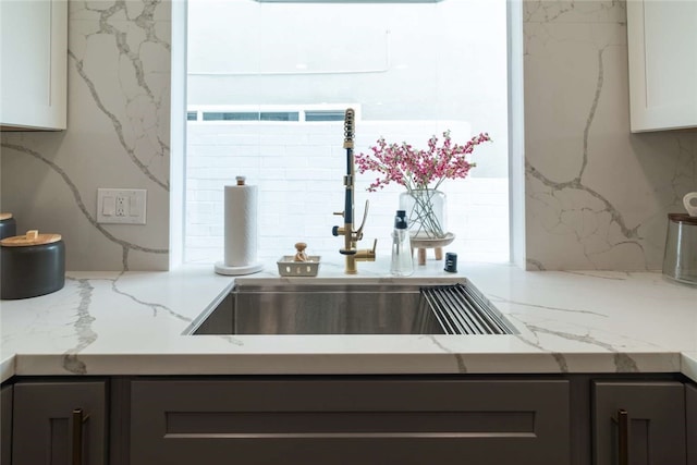 kitchen with tasteful backsplash, sink, light stone counters, and white cabinetry