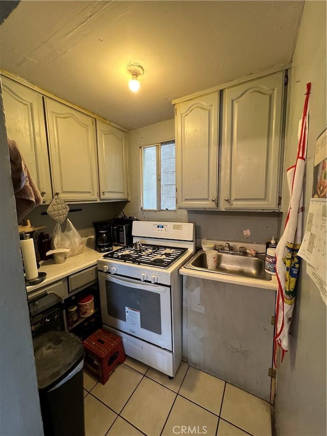 kitchen with white range with gas stovetop, white cabinets, light tile patterned flooring, and sink