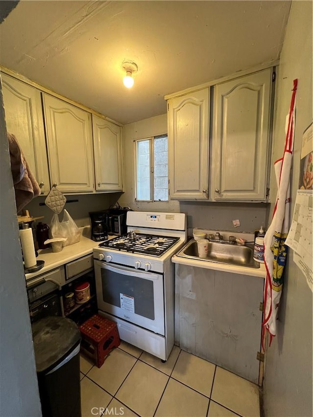 kitchen featuring a sink, light countertops, white cabinetry, white gas stove, and light tile patterned floors
