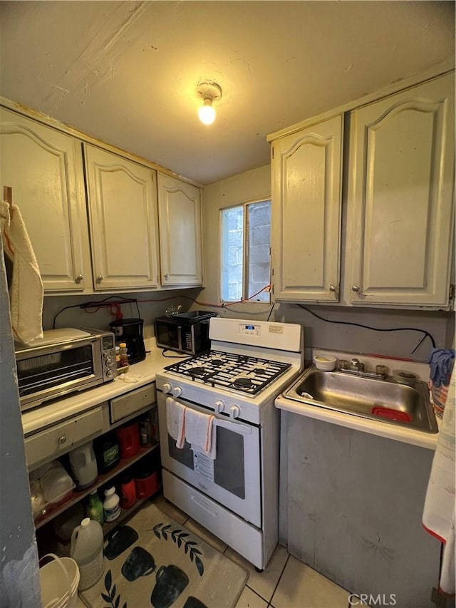 kitchen with a toaster, white range with gas stovetop, light countertops, a sink, and light tile patterned floors