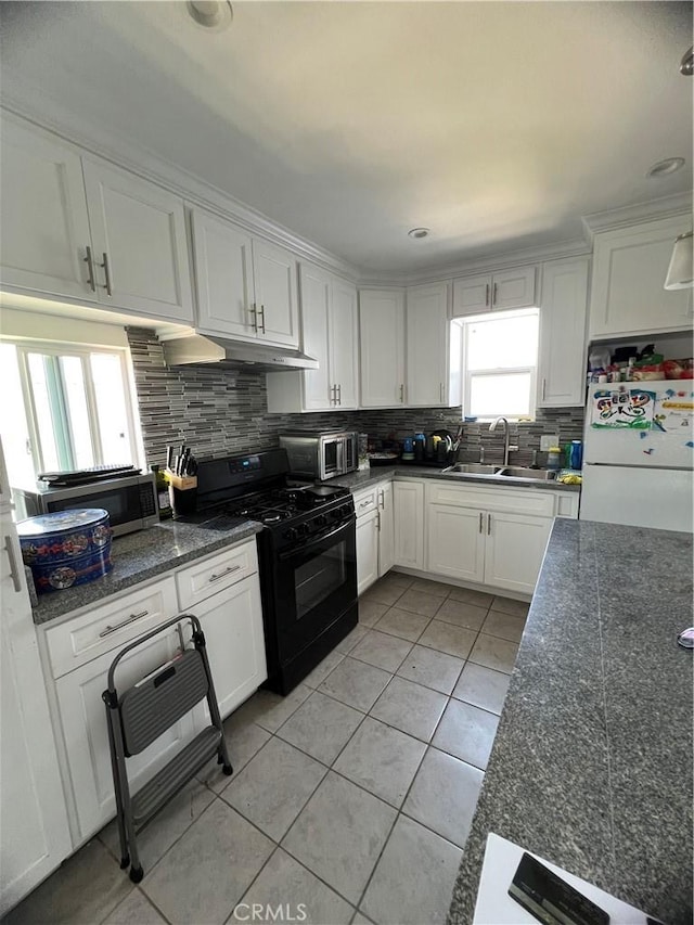 kitchen with black gas range oven, a sink, freestanding refrigerator, light tile patterned floors, and under cabinet range hood
