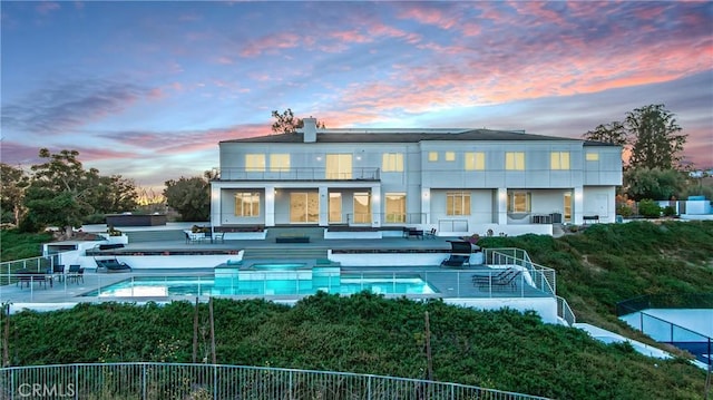 back house at dusk with a fenced in pool, a balcony, and a patio