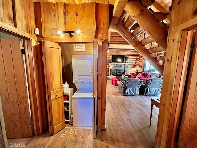 hall with light hardwood / wood-style floors, stacked washer / drying machine, and wood walls