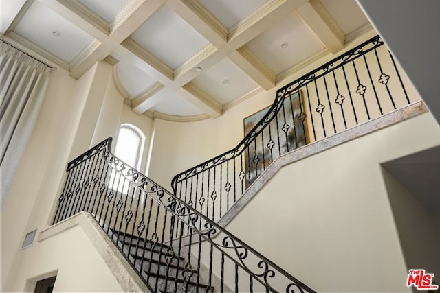 stairway with beam ceiling, coffered ceiling, and a high ceiling