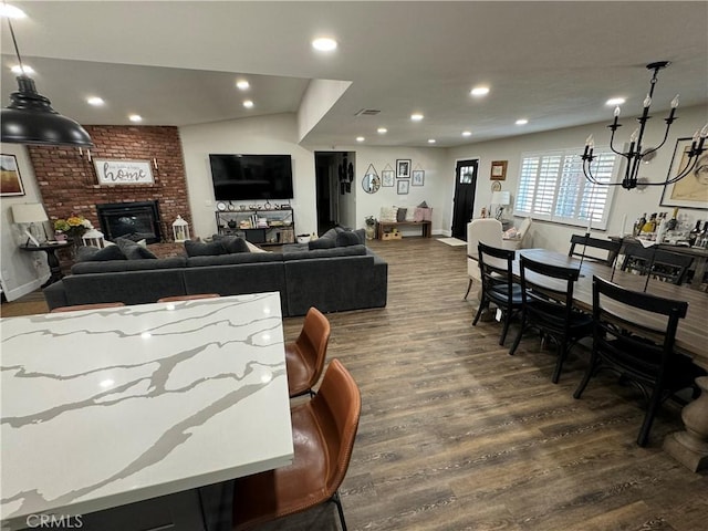 living room featuring a brick fireplace, dark wood-type flooring, and a notable chandelier