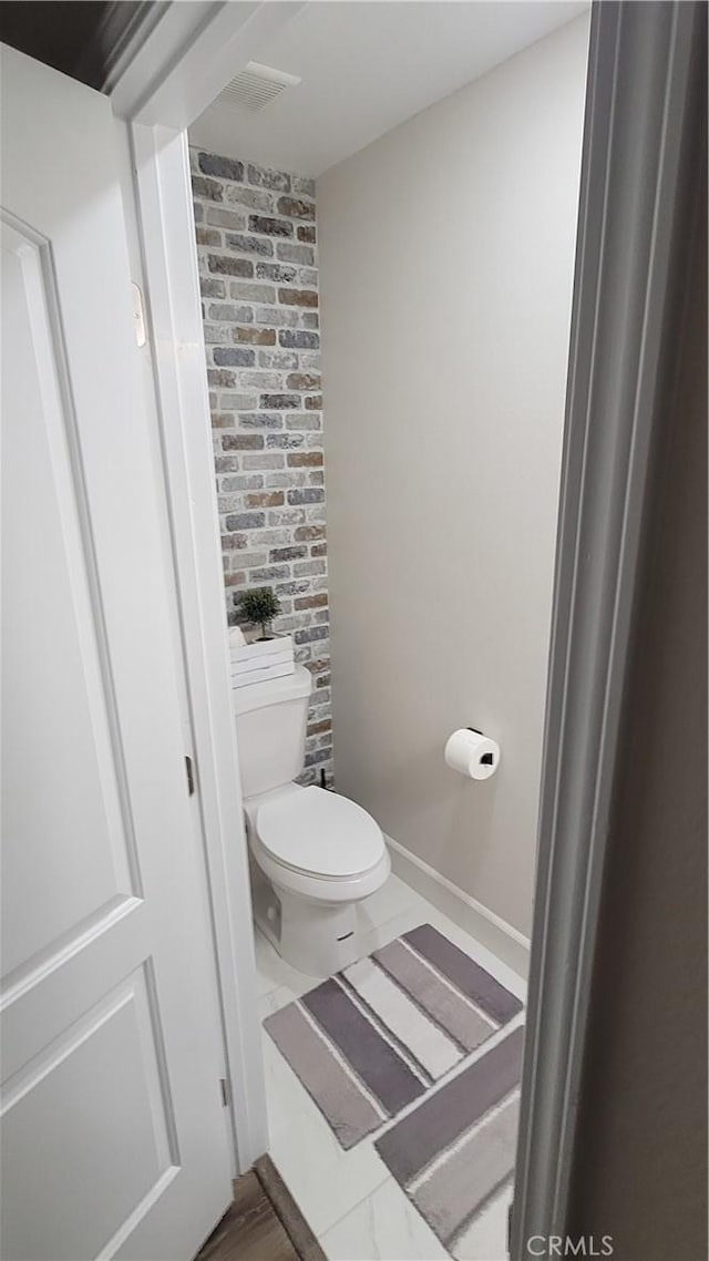 bathroom with toilet and brick wall