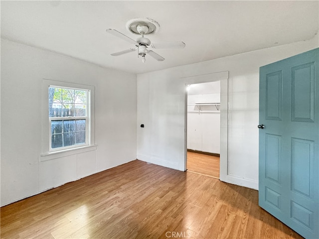 unfurnished bedroom featuring a spacious closet, light wood-type flooring, ceiling fan, and a closet