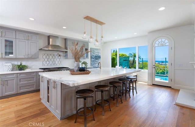 kitchen with a kitchen breakfast bar, light hardwood / wood-style floors, wall chimney range hood, and a kitchen island with sink