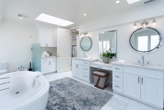 bathroom featuring a tub to relax in, vanity, a skylight, and toilet