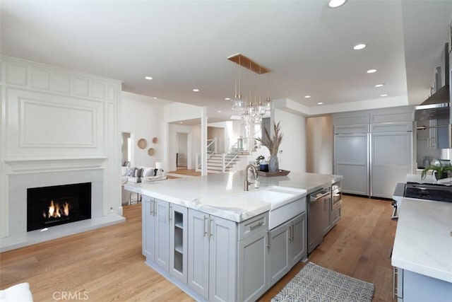 kitchen featuring hanging light fixtures, light hardwood / wood-style flooring, gray cabinets, an island with sink, and appliances with stainless steel finishes