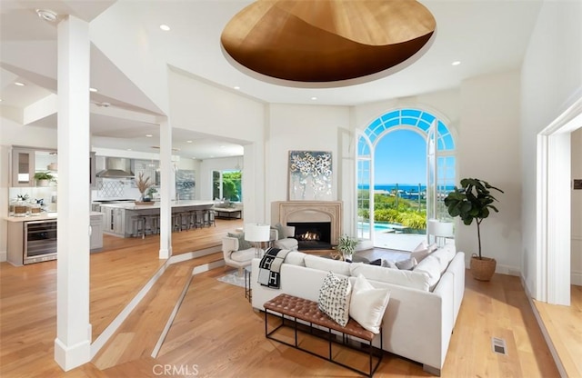 living room with a high ceiling, light hardwood / wood-style floors, beverage cooler, and a tray ceiling