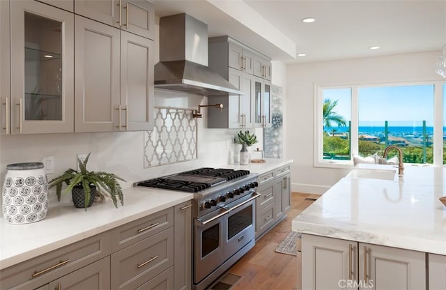 kitchen with sink, wall chimney exhaust hood, double oven range, light hardwood / wood-style floors, and gray cabinets