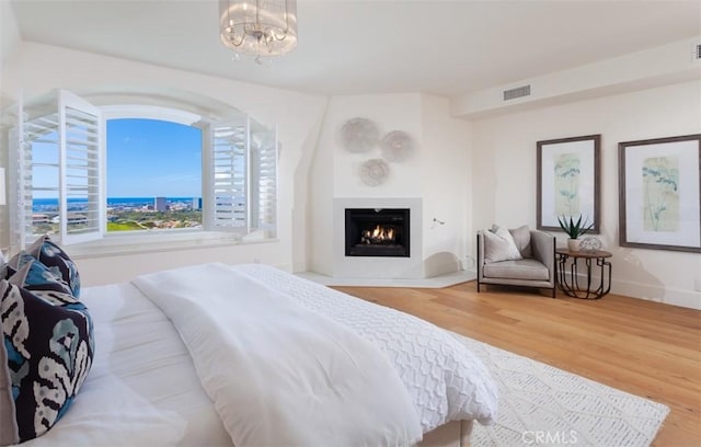 bedroom featuring a large fireplace, wood-type flooring, and a notable chandelier