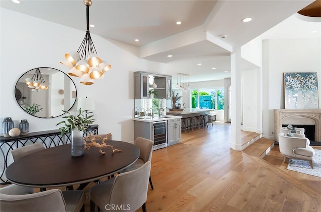 dining space with light wood-type flooring, sink, wine cooler, and an inviting chandelier