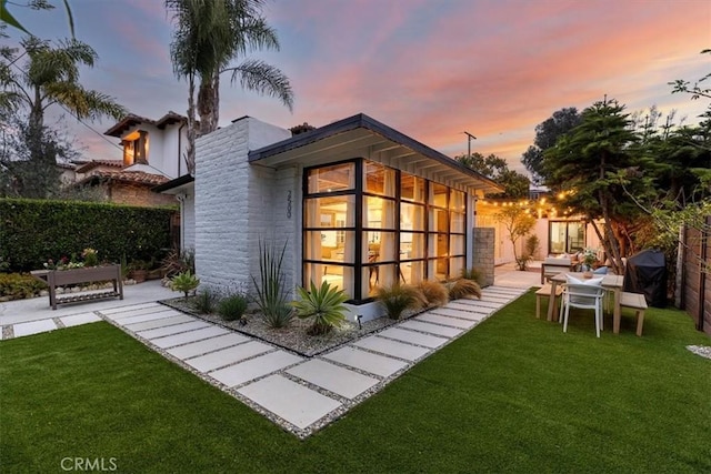 back house at dusk featuring a lawn and a patio