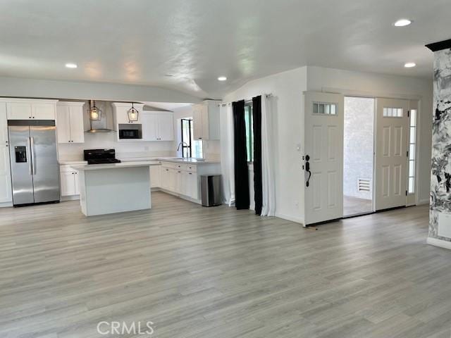 kitchen featuring stove, stainless steel fridge with ice dispenser, wall chimney exhaust hood, light hardwood / wood-style floors, and white cabinetry