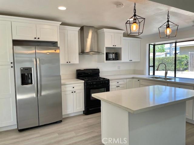 kitchen featuring wall chimney range hood, sink, black appliances, decorative light fixtures, and white cabinets