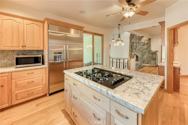 kitchen featuring light stone countertops, a center island, stainless steel appliances, light brown cabinetry, and light hardwood / wood-style floors