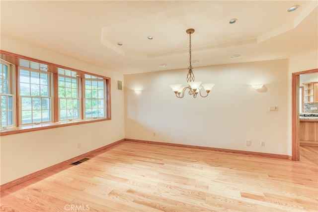 empty room featuring a raised ceiling, light wood-type flooring, and a chandelier